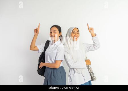 due ragazze della scuola superiore che trasportano le borse con il dito che punta in su Foto Stock