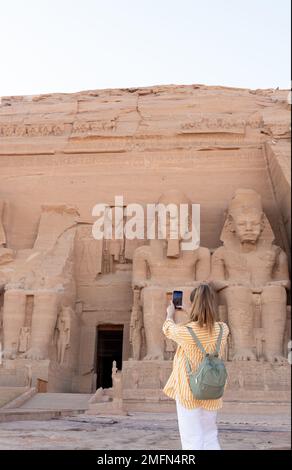 Vista verticale di una donna turistica a ritroso che scatta foto per i social media al tempio di Abu simbel in Egitto, Africa Foto Stock