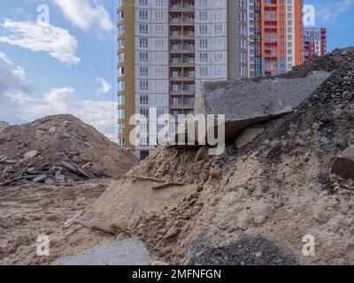 Un edificio con mucchi di sabbia e un enorme blocco di cemento in primo piano e nuovi alti edifici sullo sfondo a Kyiv, Ucraina. Nuovo distretto. Foto Stock