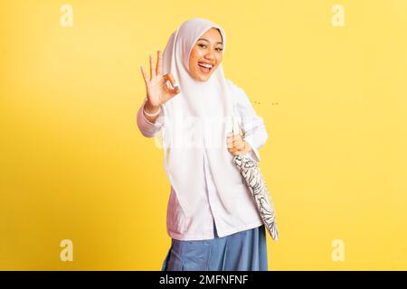 Ragazza velata indonesiana in uniforme con un gesto di mano OK Foto Stock