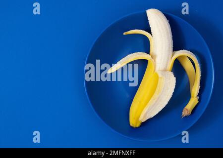 Banana semi sbucciata su sfondo blu scuro Foto Stock