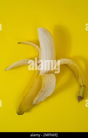 Banana semi sbucciata su sfondo giallo Foto Stock