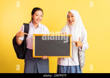 due ragazze della scuola superiore che trasportano una lavagna con il dito di puntamento Foto Stock