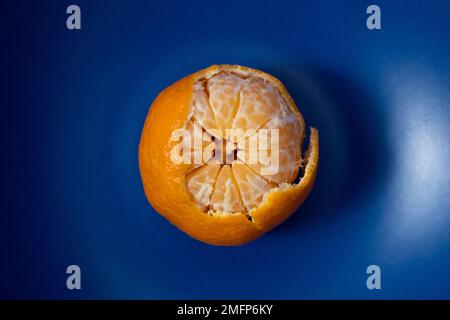 Vista ravvicinata del tangerino parzialmente sbucciato sulla piastra blu scuro Foto Stock
