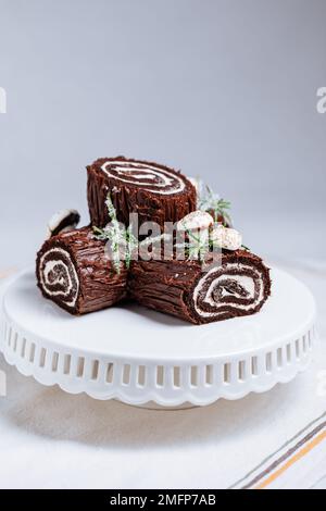 Dessert francese chiamato Yule log o bûche de Noël con funghi merengue e foglie in cima alla vetrata al cioccolato. Posto di fronte all'albero di Natale. Dic Foto Stock