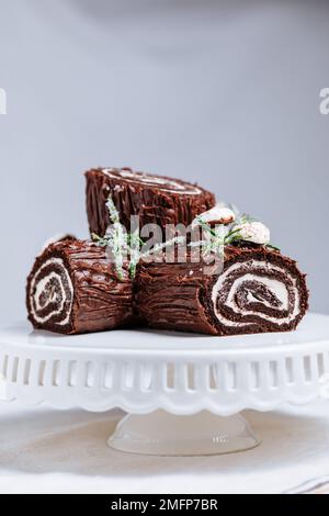 Dessert francese chiamato Yule log o bûche de Noël con funghi merengue e foglie in cima alla vetrata al cioccolato. Posto di fronte all'albero di Natale. Dic Foto Stock