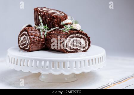 Dessert francese chiamato Yule log o bûche de Noël con funghi merengue e foglie in cima alla vetrata al cioccolato. Posto di fronte all'albero di Natale. Dic Foto Stock