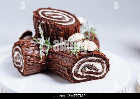 Dessert francese chiamato Yule log o bûche de Noël con funghi merengue e foglie in cima alla vetrata al cioccolato. Posto di fronte all'albero di Natale. Dic Foto Stock