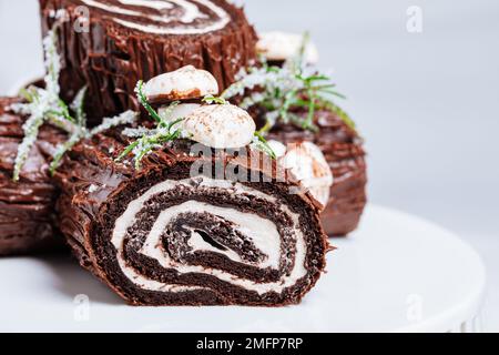 Dessert francese chiamato Yule log o bûche de Noël con funghi merengue e foglie in cima alla vetrata al cioccolato. Posto di fronte all'albero di Natale. Dic Foto Stock