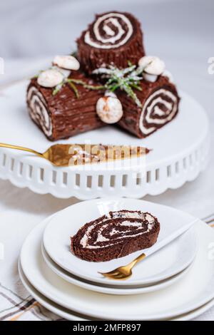 Dessert francese chiamato Yule log o bûche de Noël con funghi merengue e foglie in cima alla vetrata al cioccolato. Posto di fronte all'albero di Natale. Dic Foto Stock