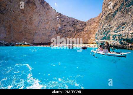 Splendida vista delle barche che porta i turisti al vecchio relitto arrugginito incagliato sulla spiaggia Navagio sull'isola di Zante in Grecia, circondato da alte scogliere Foto Stock