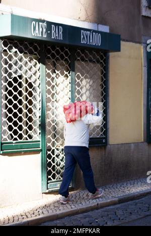 Un uomo per le strade della città di Lisbona porta sulle spalle un sacco pieno di cipolle Foto Stock