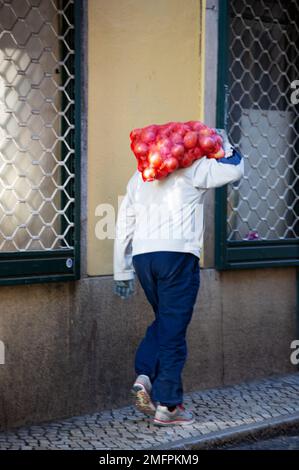 Un uomo per le strade della città di Lisbona porta sulle spalle un sacco pieno di cipolle Foto Stock