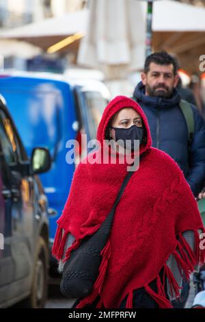 Donna con abiti invernali tradizionali e maschera protettiva cammina per le strade di Lisbona Foto Stock