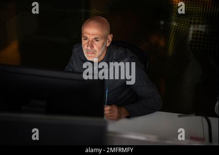 Foto di serio uomo d'affari premuroso seduto al tavolo con il computer in ufficio in tarda serata. Foto Stock
