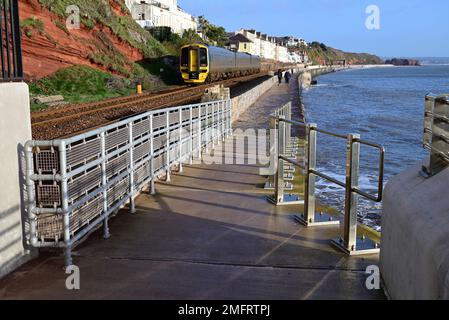 Un treno locale passando per i Cottages della Guardia Costiera, Dawlish, dove la nuova parete del mare (2022) si unisce all'originale parete del mare. Foto Stock