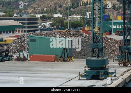 Vista sul cumulo di rottami metallici e gru da carico verdi situate nel porto pronte per il carico sulle navi. Foto Stock