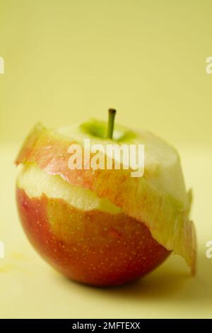 Primo piano di una mela Braeburn con una parte della pelle sbucciata su uno sfondo semplice Foto Stock