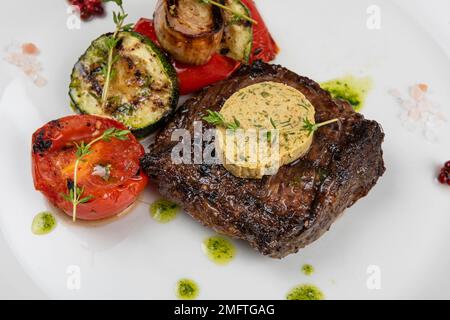 Bistecca alla griglia di lombata di angus nero con verdure su piatto bianco su sfondo di legno nero Foto Stock