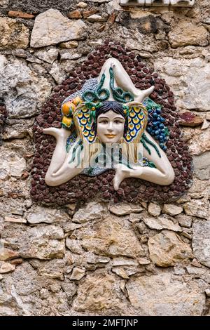 Muro di pietra in uno dei vicoli della meta turistica di Taormina con una Trinacria, simbolo a tre zampe della Sicilia. Foto Stock
