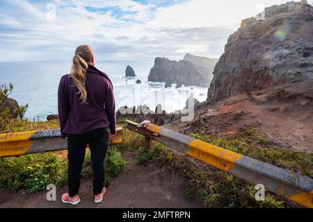 Giovane donna che si affaccia sul mare, Miradouro da Ponta do Rrosso, costa frastagliata con formazioni rocciose, Capo Ponta de Sao Lourenco, Madeira, Portogallo Foto Stock