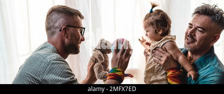 Coppia gay maschile con la bambina adottata a casa - due bei padri che giocano con la loro figlia - famiglia LGBTQ+ a casa - Diversity Concept e LGBT Foto Stock