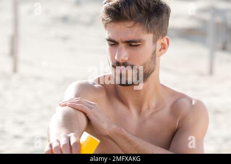 uomo che applica lozione di crema solare sul suo corpo Foto Stock