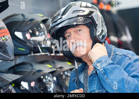 uomo anziano che sceglie il casco del motociclo al deposito Foto Stock