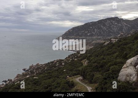 Paesaggio collinare appena fuori Phan Rang Vietnam, con cielo nuvoloso in una giornata parzialmente soleggiata con le montagne che scendono verso il mare Foto Stock