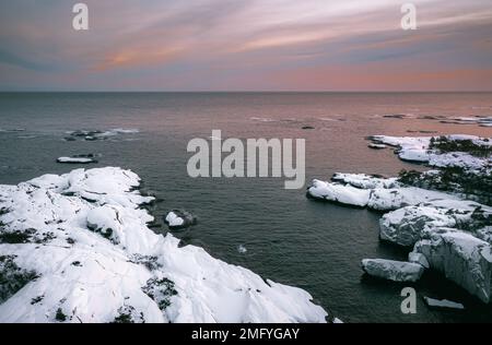 Vista aerea della costa innevata del mare, cielo colorato al tramonto in Norvegia. Paesaggio solare invernale con ghiaia gelida, fiordo e linea dell'orizzonte. Vista dall'alto di N Foto Stock