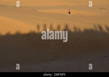 Una persona in lontananza sulle dune di sabbia rossa a Mui NE, provincia di Phan Thiet, Vietnam, con ombre di persone in cima alle dune sottostanti. Foto Stock