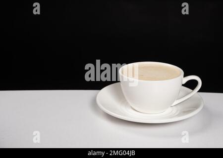 Caffè con crema di latte, cappuccino in una tazza di ceramica bianca su sfondo bianco nero, copiare la posizione per il testo Foto Stock