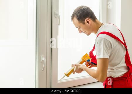 Addetto alle costruzioni che mette in casa il nastro di schiuma sigillante sulla finestra Foto Stock