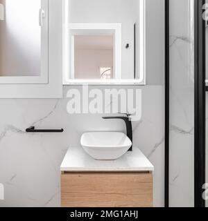 Il bagno luminoso vanta uno stile elegante e minimalista, con un lavabo bianco scintillante posto contro uno splendido specchio con cornice nera, a creare un moderno e Foto Stock