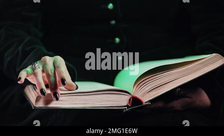 Le mani di una donna strega nera si capovolge sulle pagine del vecchio libro magico. Mago, incantesimi Foto Stock