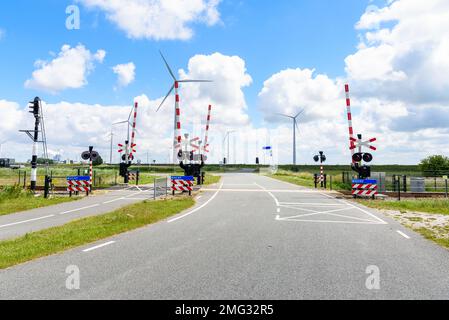 Level Crossing con segnali e segnali di avvertimento lungo una strada e una pista ciclabile nella campagna dei Paesi Bassi. Una fattoria eolica è sullo sfondo. Foto Stock