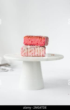 Lamingtons rosa su una torta di marmo bianco stand lamingtons australiani lampone, piccole torte coperte di noci di cocco essiccate Foto Stock