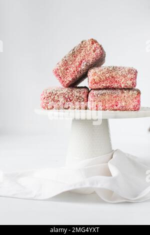 Lamingtons rosa su una torta di marmo bianco stand lamingtons australiani lampone, piccole torte coperte di noci di cocco essiccate Foto Stock