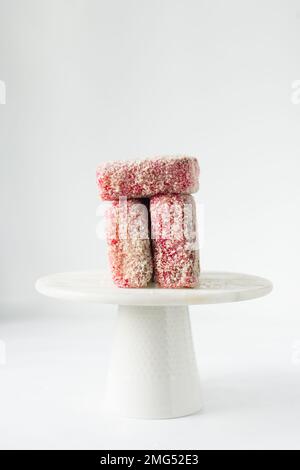 Lamingtons rosa su una torta di marmo bianco stand lamingtons australiani lampone, piccole torte coperte di noci di cocco essiccate Foto Stock