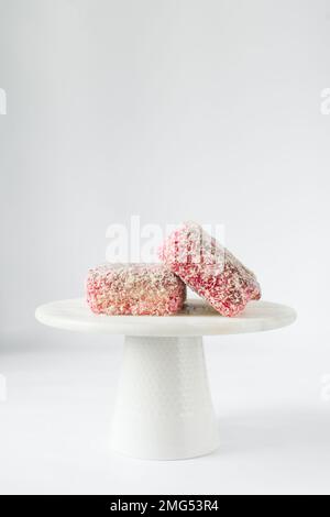 Lamingtons rosa su una torta di marmo bianco stand lamingtons australiani lampone, piccole torte coperte di noci di cocco essiccate Foto Stock