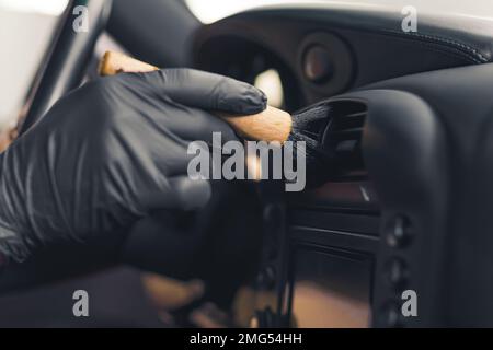 Primo piano della mano indossata all'interno dell'auto spazzolando le bocchette di ventilazione sul cruscotto. Lavoro di precisione. Concetto di dettaglio degli interni dell'auto. Scatto orizzontale in interni. Foto di alta qualità Foto Stock