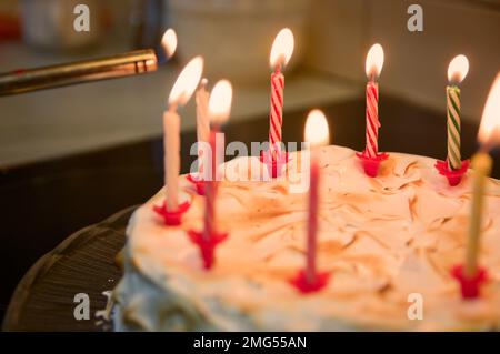 Primo piano di una torta di compleanno decorata con candele accese utilizzando un bruciatore da cucina Foto Stock