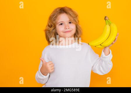 Bambino tenere banana in studio. Studio ritratto di carino ragazzo con banane isolato sul giallo. Foto Stock