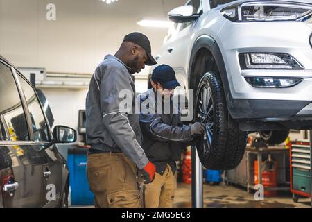 Immagine media di due meccanici che riparano una ruota di un'auto. Concetto di officina di riparazione. Foto di alta qualità Foto Stock