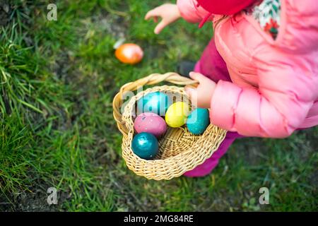 Il bambino raccoglie le uova di Pasqua colorate nel cestino. Concetto di caccia all'uovo di Pasqua Foto Stock