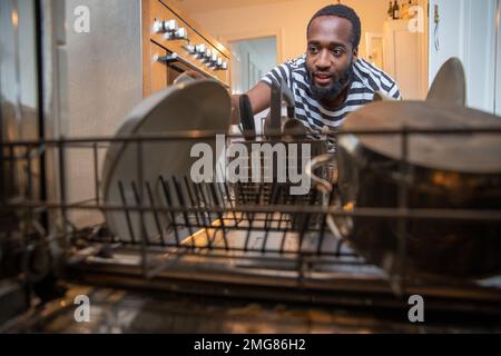 L'uomo afroamericano toglie i piatti dalla lavastoviglie dopo il lavaggio, concetto di lavoro domestico Foto Stock