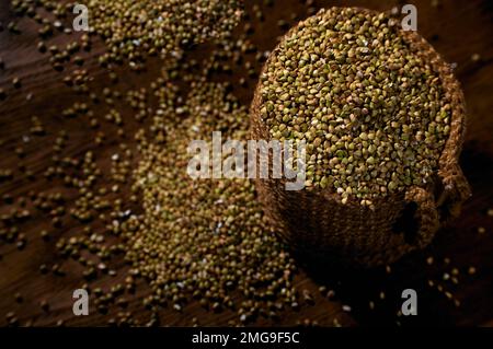 Grani di grano saraceno crudo verde in un sacchetto di iuta su un tavolo di legno Foto Stock