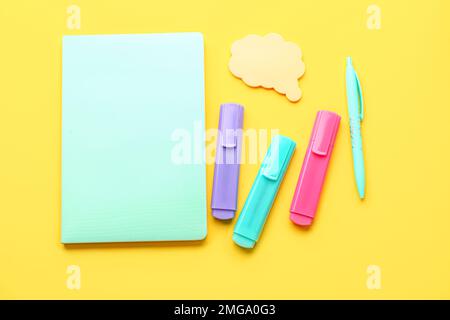 Notebook, penna, pennarelli e note adesive su sfondo giallo Foto Stock
