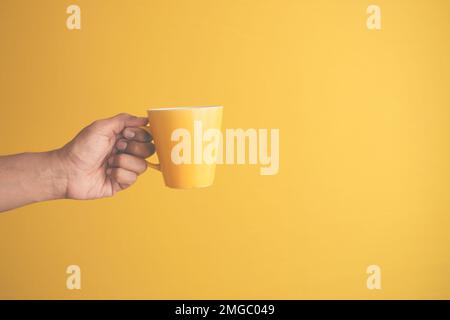 primo piano della mano dell'uomo che tiene la tazza di colore giallo Foto Stock