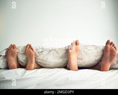 Lascia annullare oggi e rimanere a letto. un paio di piedi che si scopano da sotto le lenzuola. Foto Stock